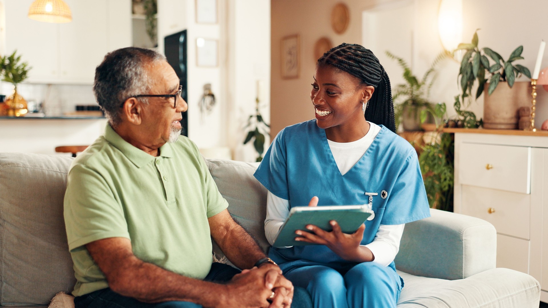 Nurse, senior man and tablet on sofa with smile for wellness, medical update and report in lounge. Woman, caregiver and elderly patient on couch with digital touchscreen, app and healthcare results