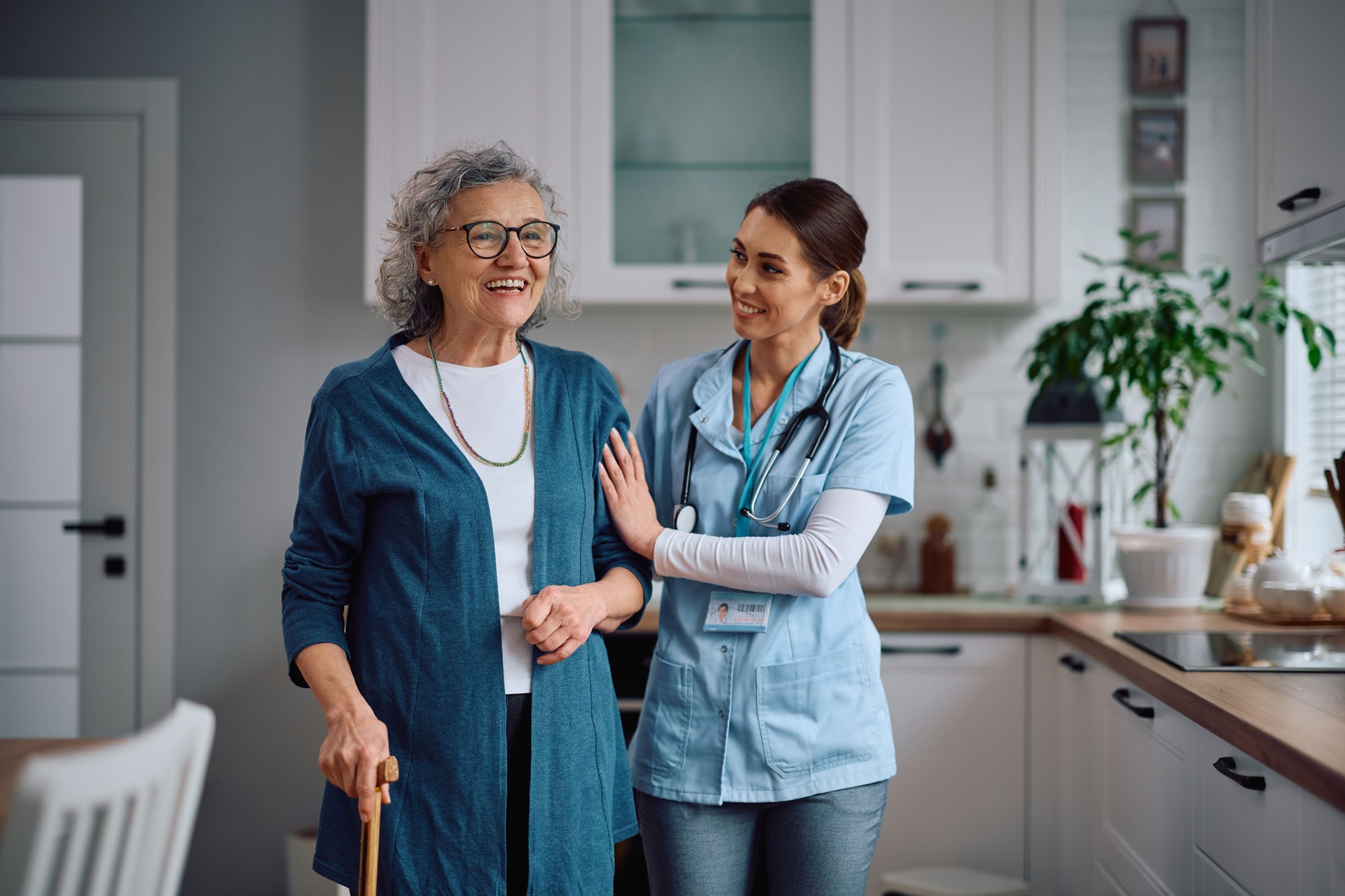 Happy senior woman walking with help of female caregiver during a home visit.